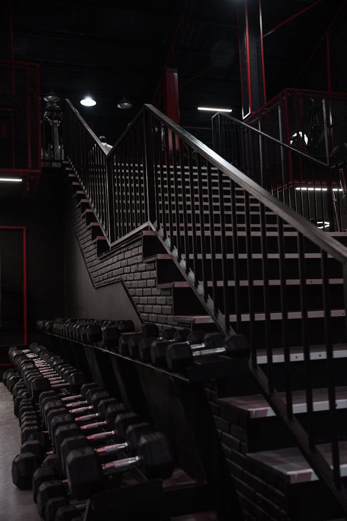 A sleek, industrial-style gym interior featuring a staircase and stacked dumbbells.