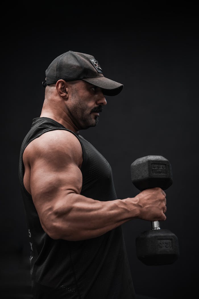Strong man performing bicep curls with a dumbbell, focus on muscle definition.